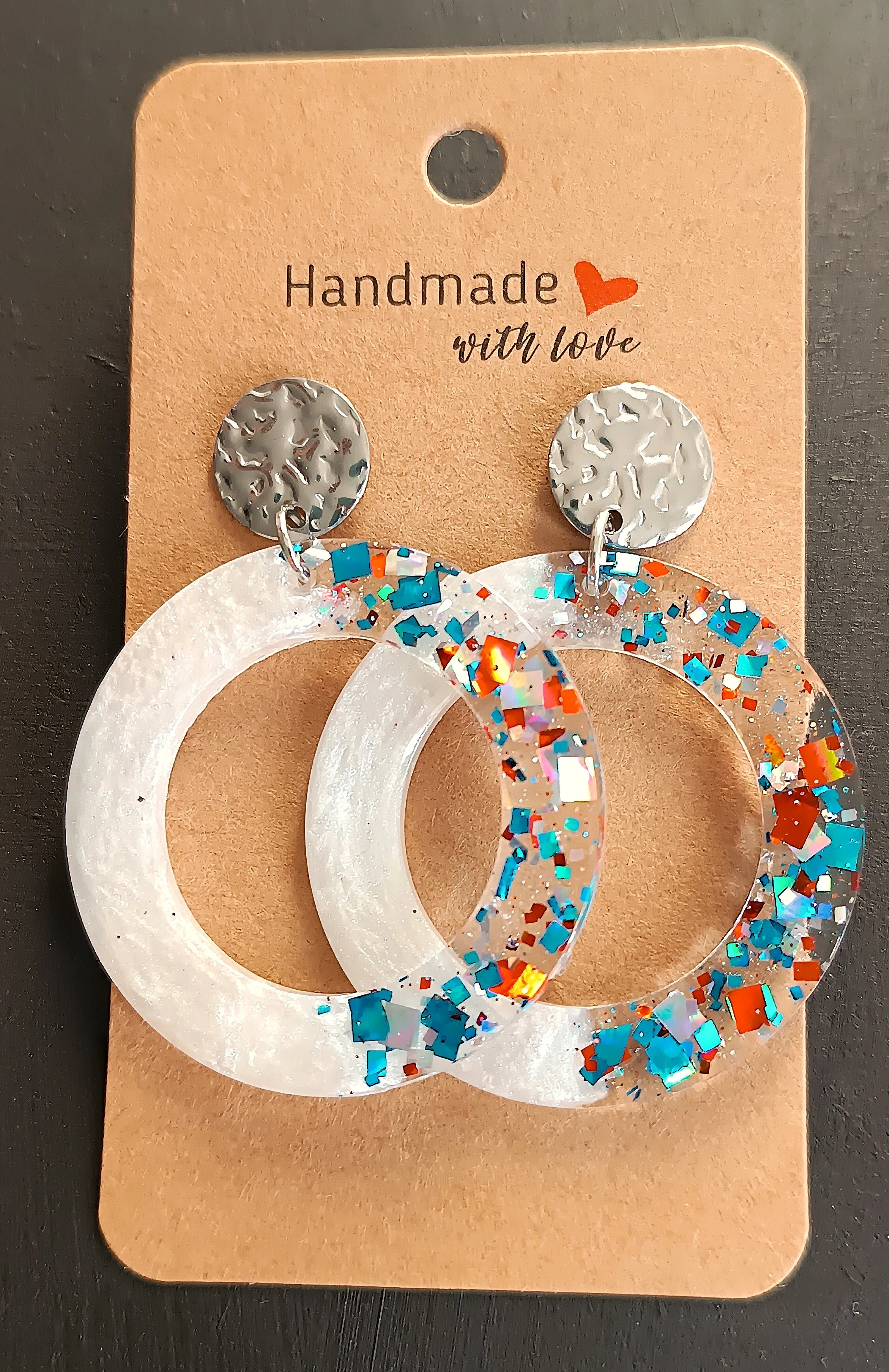 Boucles d’oreilles rondes en résine UV  avec paillettes bleu, argent et brun, bijoux faits main, sur un carton de présentation